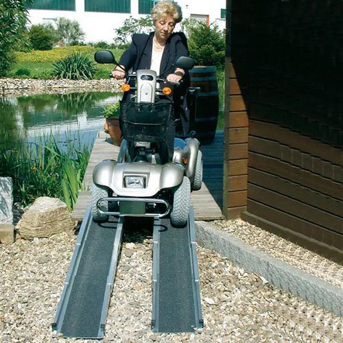 Eine Scooterrampe aus rutschfestem Alluminium über die eine ältere Dame in ihrem Scooter herunterfährt, um von ihrer Veranda herunterzukommen.jpg